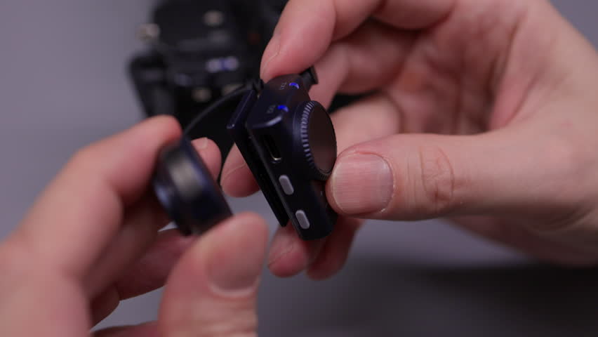 Closeup hands of professional videographer syncing wireless lavalier microphone system with camera, ensuring optimal audio quality for broadcast, interview or filmmaking in dark studio, slow motion.
