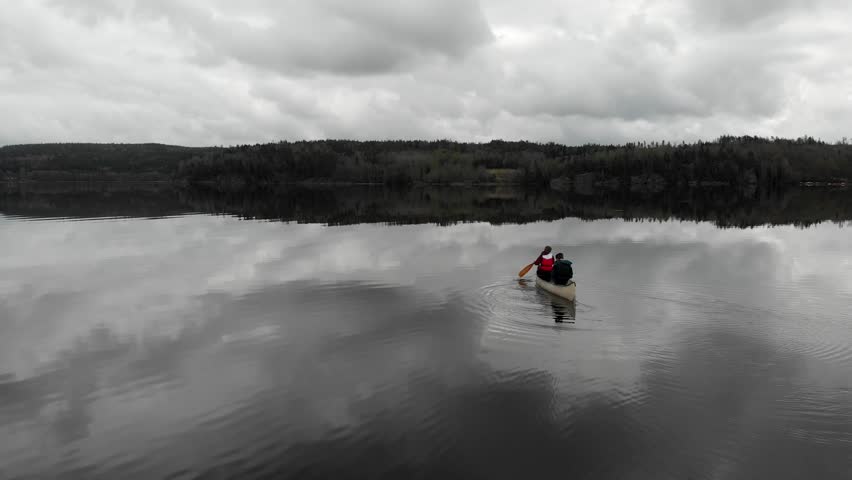 AERIAL - Following people on a canoe on a lake, clouds reflecting on it, Sweden