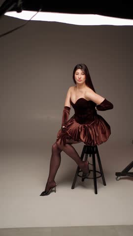 Elegant woman in velvet dress sitting on chair in studio lighting. Concept glamour model portrait.