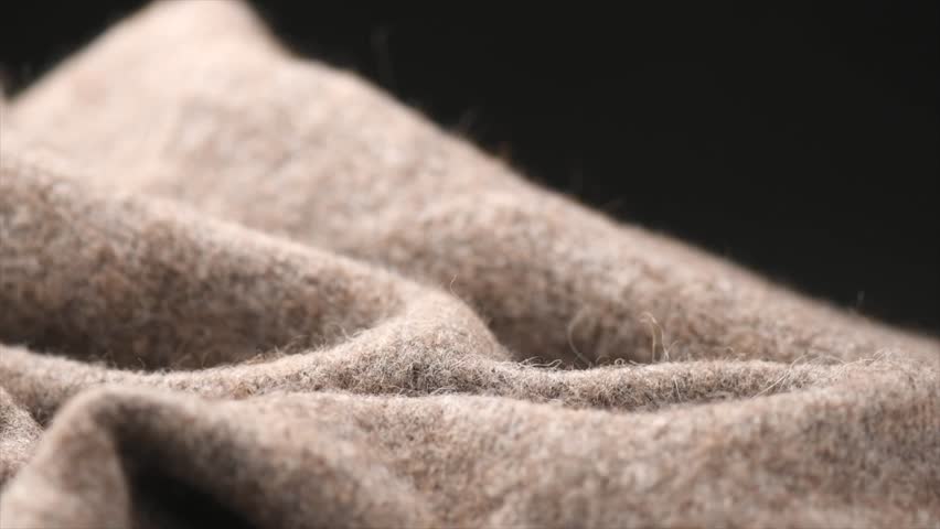 Knitted Wool over black background. Real Natural beige color craft wool mohair clothes texture closeup. Cashmere Soft and fluffy merino wool macro shot. Woolen fabric backdrop. Rotating border 