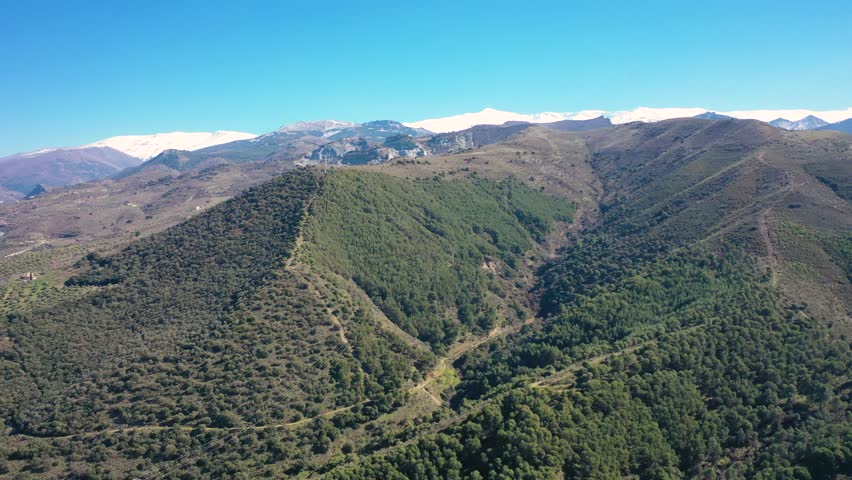 Aerial 4K video from a drone of the snow-capped mountains of the Sierra Nevada on a sunny day. In the background, the green mountains of Granada. Sierra Nevada, Granada, Andalusia, Spain.