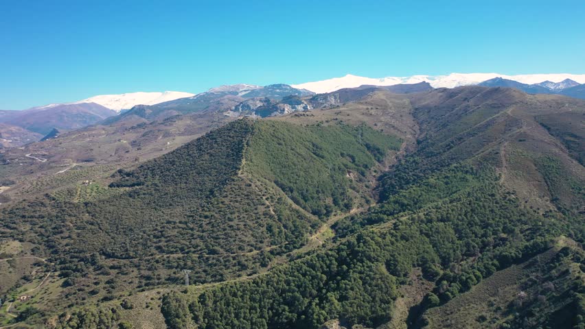 Aerial 4K video from a drone of the snow-capped mountains of the Sierra Nevada on a sunny day. In the background, the green mountains of Granada. Sierra Nevada, Granada, Andalusia, Spain.