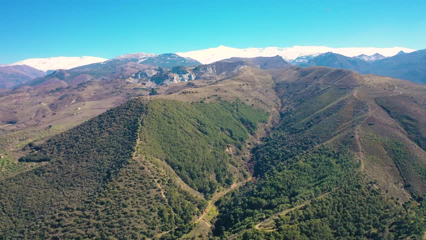 Aerial 4K video from a drone of the snow-capped mountains of the Sierra Nevada on a sunny day. In the background, the green mountains of Granada. Sierra Nevada, Granada, Andalusia, Spain.