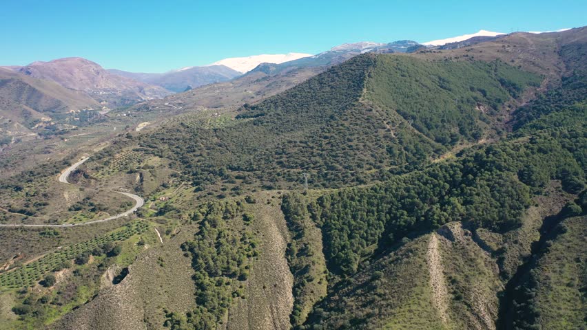 Aerial 4K video from a drone of the snow-capped mountains of the Sierra Nevada on a sunny day. In the background, the green mountains of Granada. Sierra Nevada, Granada, Andalusia, Spain.