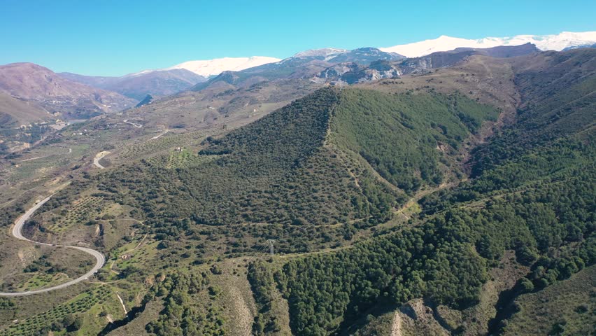 Aerial 4K video from a drone of the snow-capped mountains of the Sierra Nevada on a sunny day. In the background, the green mountains of Granada. Sierra Nevada, Granada, Andalusia, Spain.