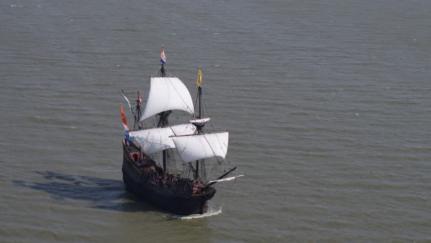 Replica of historic VOC ship sailing in open seas, Dutch flags flutter; drone