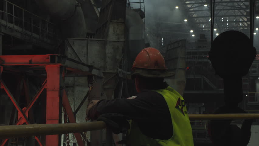 Nighttime Safety Supervisor In Protective Attire Oversees Complex Manufacturing Equipment Operations . Stock clip
