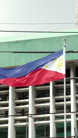 The Filipino flag waves on a flagpole against a green urban building in Manila