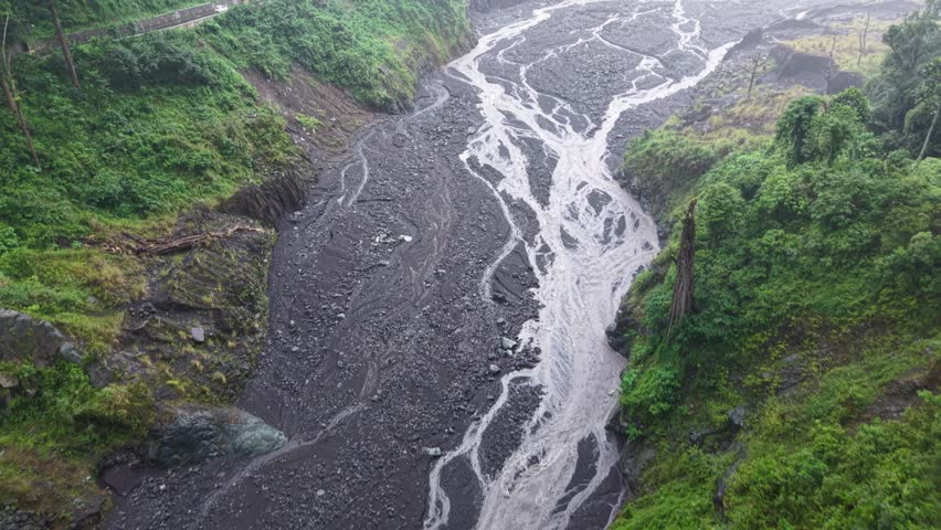 Aerial landscape showing a braided river carving a rocky riverbed between steep, vegetation covered cliffs dramatic erosion patterns and contrasting green slopes create a remote, rugged natural scene full of texture and movement.
