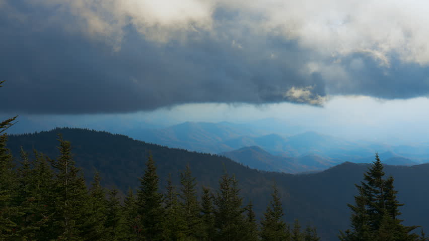 Storm clouds over layered mountain landscape. Misty blue ridges and approaching rain creating atmospheric natural background.