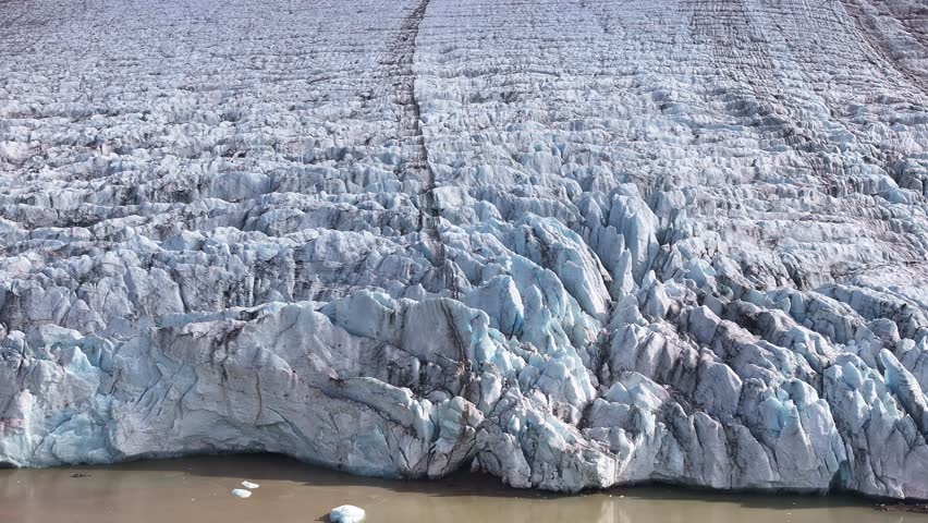 Aerial orbit shot moving from a jagged glacier to a misty fjord and rugged rocky cliffs in Greenland under desolate overcast skies.