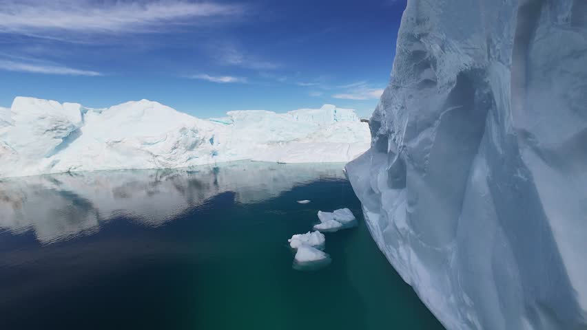 Dynamic FPV drone proximity flight maneuvering through massive, jagged icebergs in a Greenland fjord, showcasing crystalline textures and turquoise arctic waters.
