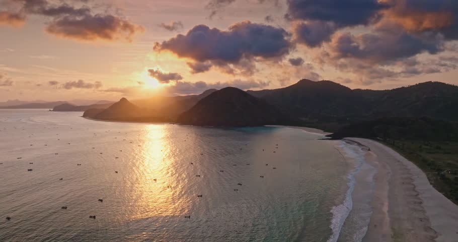 Selong Belanak Beach coastline in Lombok, Indonesia, capturing a golden sunset reflecting on the calm ocean waters with small boats scattered across the tranquil bay and mountains in the background