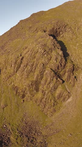 Golden light illuminates vast mountainous slopes with rugged terrain under a clear blue sky.