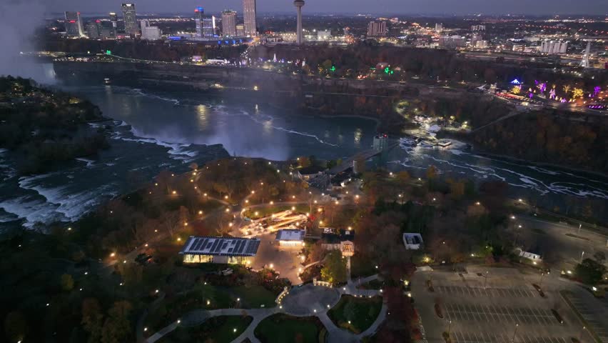 Smooth orbit shot showcasing the illuminated Niagara Falls and the surrounding city skyline showcasing Skylon Tower at twilight, 4K aerial drone footage from Ontario, Canada.