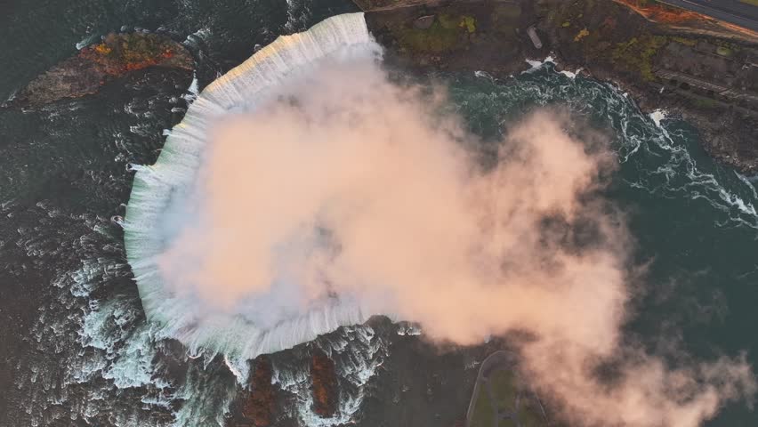 Rotating top-down timelapse drone shot of the mist rising from Niagara Falls during a majestic golden hour in Canada, 4K aerial footage.