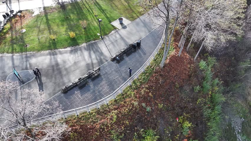 Aerial pull-out shot of a man standing on a paved walkway overlooking the Niagara River gorge in Canada during autumn, 4K.