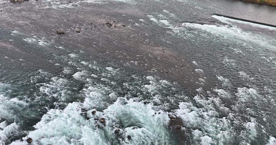 Majestic pan shot of the rushing white water rapids of the Niagara River near a hydroelectric power station in Canada, 4K aerial.