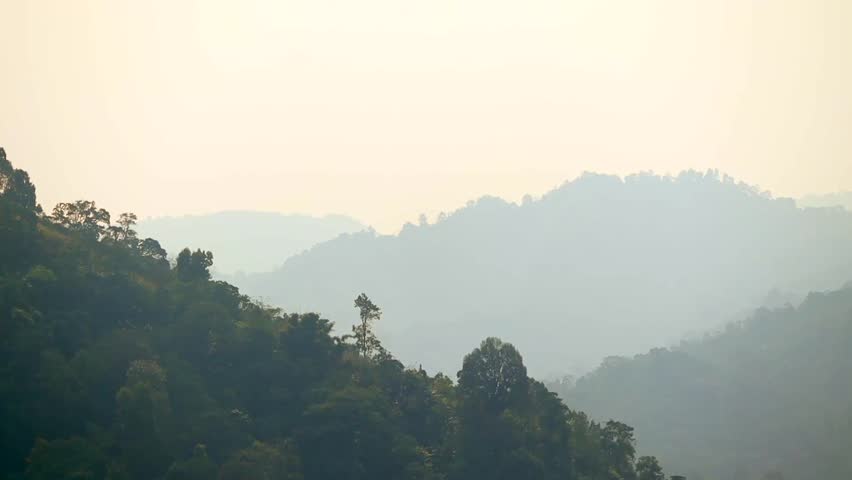 Layered mountain hills fading into soft haze beneath a warm golden sky. A tranquil natural landscape showcasing dense forest, atmospheric depth, and peaceful highland scenery.
