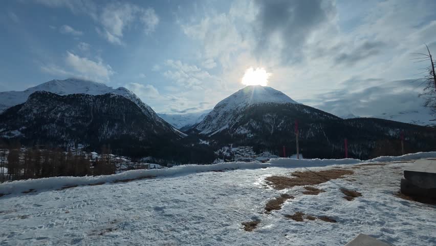 Dramatic clouds passing over a snow covered mountain valley as the sun sets behind a peak