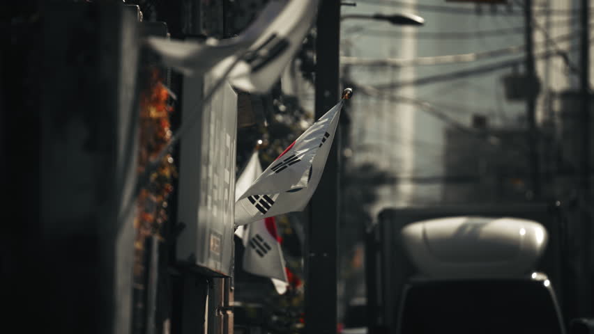 South Korean flags hanging along narrow Seoul street with dense overhead cables and CCTV camera in background