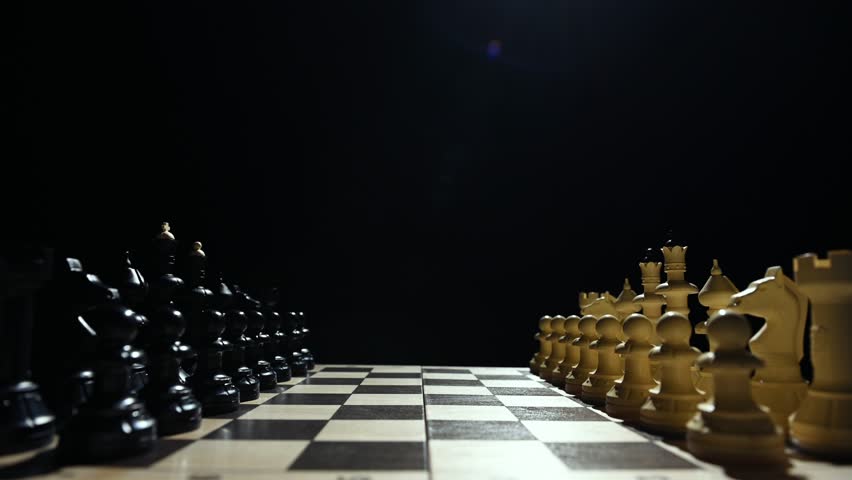 Chess pieces are facing each other on a black background. A close-up of a hand moving a white pawn 4 к