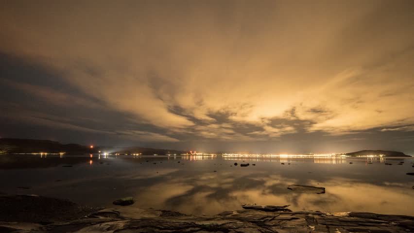 Northern lights and the moon on a cloudy night above the fjord. Tide coming in and out. Full night timelapse.
