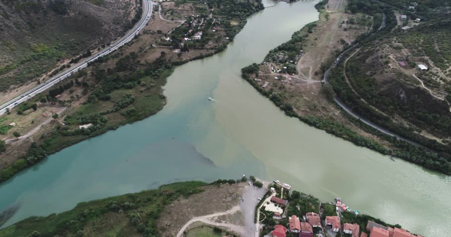 Mtskheta, Georgia - September 11, 2018: Aerial view of a river confluence showing two water colors meeting in a valley with hills, vegetation, roads and highway along the shoreline.