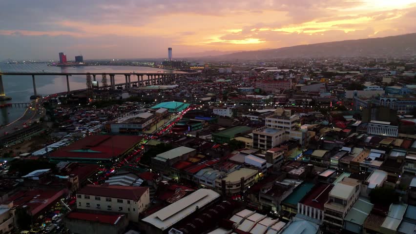 Cinematic aerial view of the golden sunset over the bustling urban skyline and coastal waters of Cebu City in the Philippines