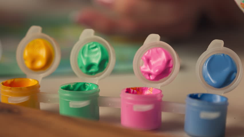 Small Acrylic Paint Pots With Lids Open And Paintbrushes Dipping. close-up shot
