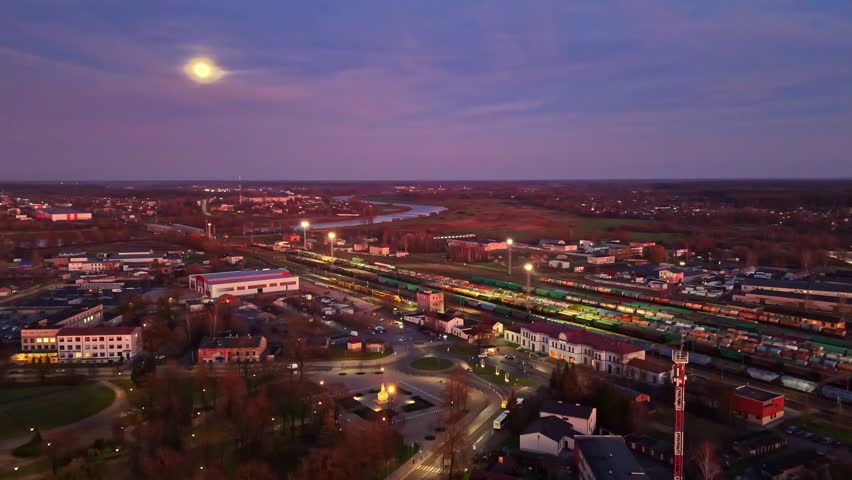 Aerial: train station at sunset with freight trains and the moon shining, establishing drone shot
