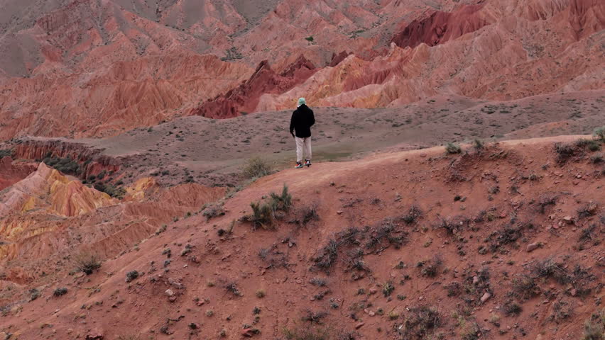 Traveler overlooking red clay canyon landscape from high ridge aerial view