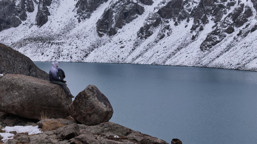 Hiker Sitting Above Alpine Lake in Winter Drone View