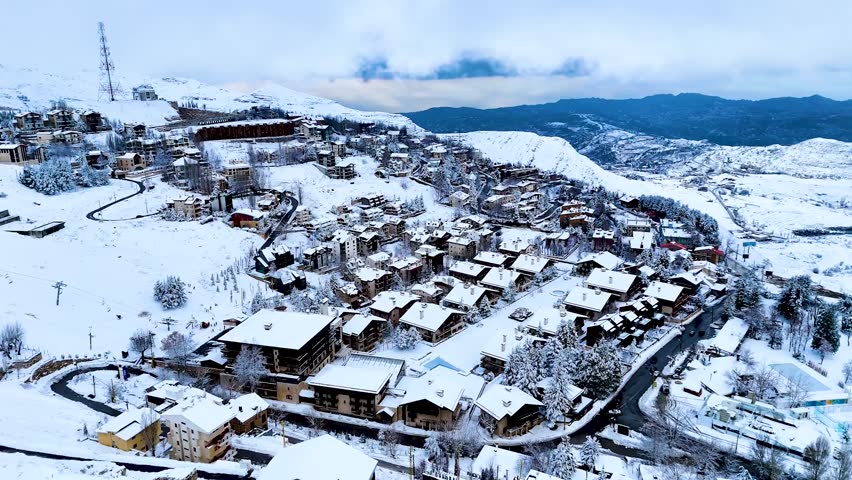 Drone Aerial shot of Kfardebian village blanketed in snow with mountain backdrop. Winter tourism destination featuring chalets, hotels and alpine landscape in Lebanon.