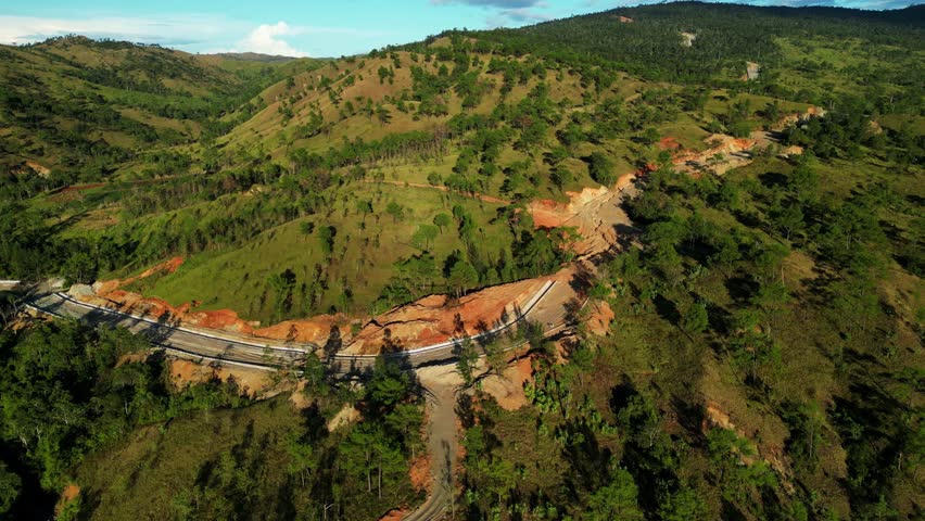Downward shot highlighting unfinished red orange road perfectly positioned in the middle of radiant mountains Daang Kalikasan Aguilar Mangatarem Pangasinan Philippines