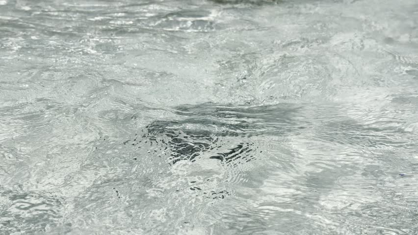 Turbulent water forms a whirlpool in a clear blue pool. 