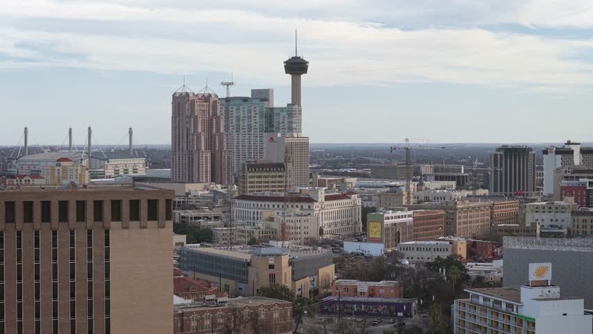 Aerial drone shot of downtown San Antonio with many buildings on a slightly cloudy day. Showing bustling city life and Texas downtown setting.