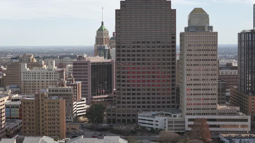 Aerial drone shot of downtown San Antonio with many buildings on a slightly cloudy day. Showing bustling city life and Texas downtown setting.