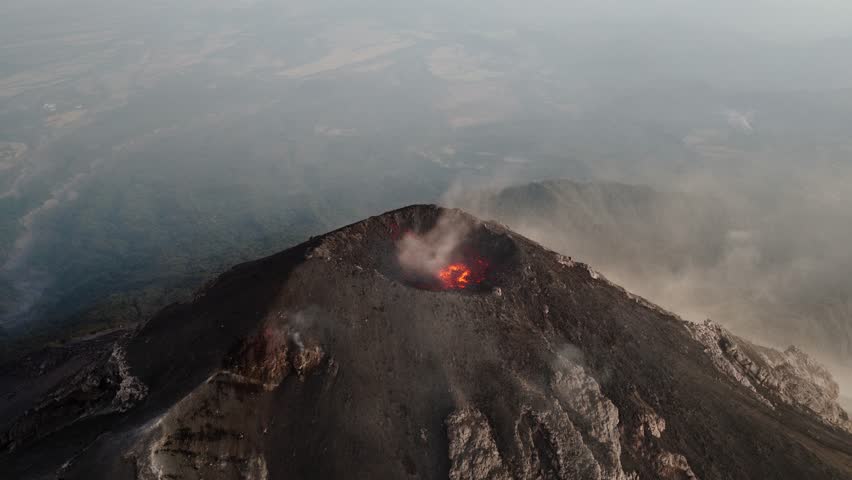 Aerial view of Fuego Volcano crater with glowing lava and steam rising over the surrounding Guatemalan landscape.