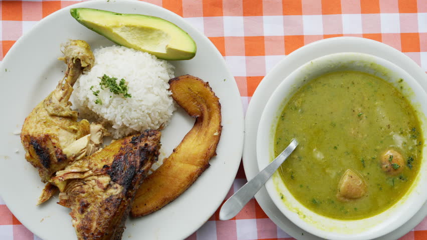 A close-up shot of Sancocho de Gallina and traditional sides like rice, avocado, and fried plantain served on a vibrant checkered tablecloth. Perfect for foodies and culinary enthusiasts.