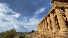Cinematic left-to-right moving shot of the ancient Greek ruins in Agrigento, Sicily, showcasing the majestic Doric columns of the Valley of the Temples under a dramatic blue sky. The camera movement h - Powered by Shutterstock - Get 15% off with code: PIKWIZARD15
