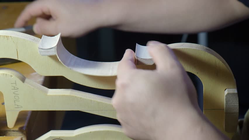 Raw violin plate edge is precisely measured with caliper by luthier to control thickness and refine maple contour during instrument construction inside workshop, close up static shot.