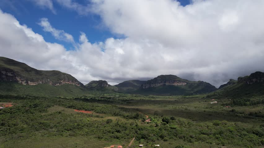 Flying over green fields towards the mountains with clouds passing by