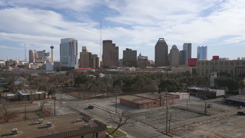 Aerial drone shot of downtown San Antonio with many buildings on a slightly cloudy day. Showing bustling city life and Texas downtown setting.