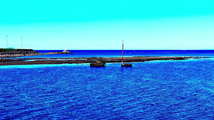 Aerial dolly forward toward a historic shipwreck SS Kaffir off Ayr, Scotland, UK, set in vivid blue coastal water near the harbour breakwater, with calm ripples and mast remains above the surface