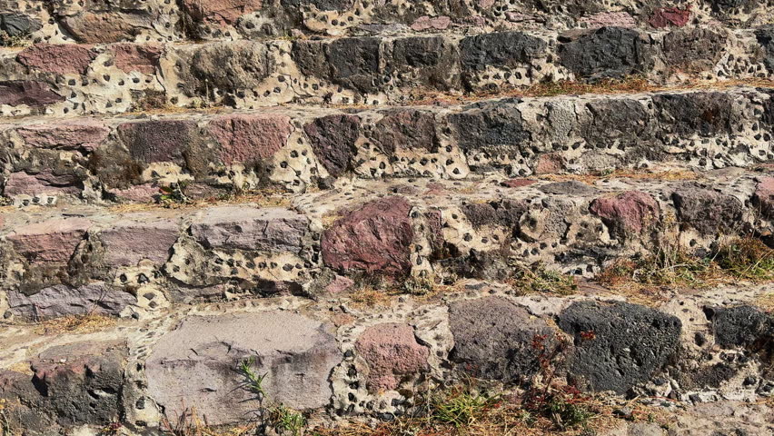 View from Teotihuacan after climbing pyramid stairs, overlooking dry grass terraces and stone ruins with a distant pyramid and mountains under clear blue sky.