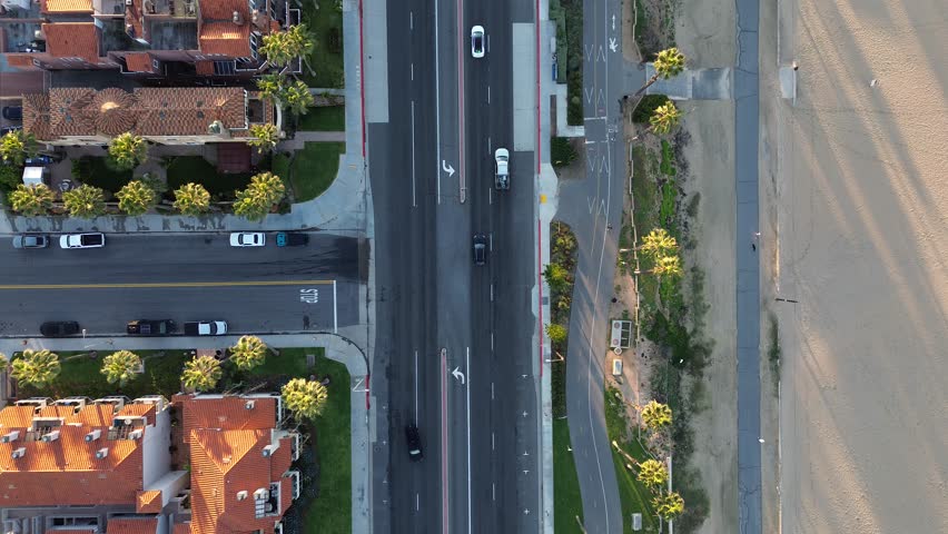 PCH at 15th St borders beachfront greenbelt, bike path leading toward central Huntington City Beach zone. Textured sand, solar panels, long palm shadows, clean coastal grid. Huntington Beach, CA. USA