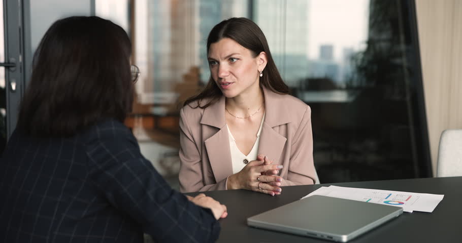 Two businesswomen sitting at table, making deal, starting collaboration, shaking hands during formal meeting in corporate office. Trust in business, successful negotiation outcome, agreement sign