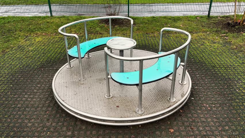 Empty playground merry-go-round rotating slowly outdoors on a cloudy day after rainfall. Wet metal surface and damp ground create a quiet, melancholic atmosphere. Concept of childhood, solitude, nostalgia, urban environment, and moody weather.
Static shot with natural lighting and realistic ambient conditions