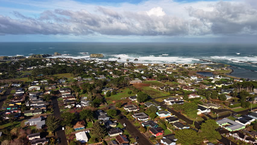 Residential homes in Bandon Oregon, drone orbit above town with ocean and sea stacks in distance.